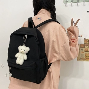 Close-up of black nylon backpack with a cute white plush bear pendant and side pockets