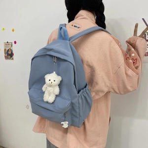 Detail view of the misty blue nylon backpack featuring side pockets and a cute bear charm