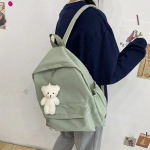 Sage green nylon backpack featuring a white plush bear charm on a female model