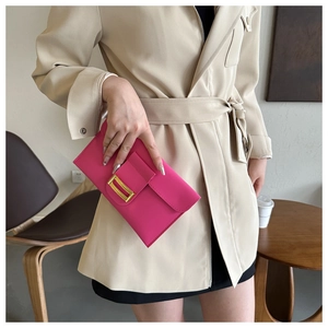Magenta envelope clutch bag with gold trim held by a model in a beige trench coat