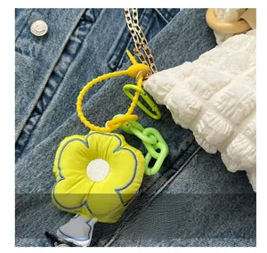 Detailed shot of yellow flower charm with blue stitching on a white textured shoulder bag