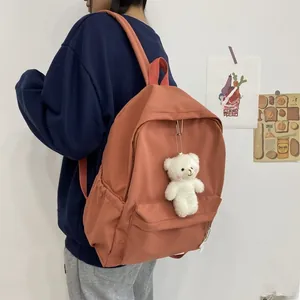Detail view of brick orange nylon backpack with side pocket and plush bear charm