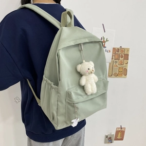 Light green nylon backpack detail with a cute white plush bear charm on the front pocket