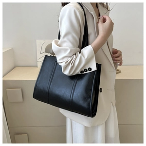 Detail of a black oil-wax leather tote bag with vertical stitching and long shoulder straps