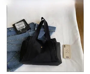 Vista detallada de la bolsa tote de lona negra con correa ancha y bolsillo lateral