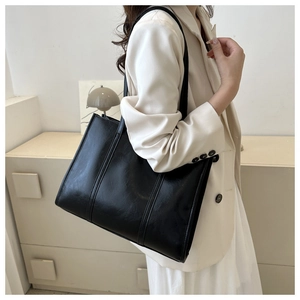Close-up of black oily leather tote bag with vertical stitching and long shoulder strap