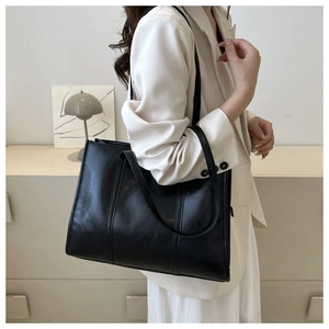 Close-up of a large black faux leather tote bag with glossy texture for daily office commuting