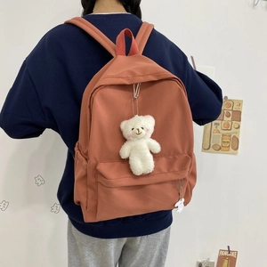Orange nylon backpack with teddy bear pendant shown on model in a minimalist setting