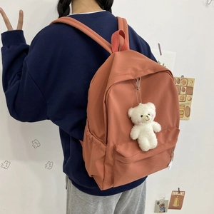 Back view of a coral orange nylon backpack with a cute white teddy bear charm on the back