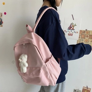 Side view of a light pink nylon backpack featuring a plush bear charm and padded straps
