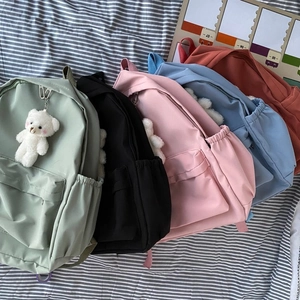 Flat lay of colorful nylon backpacks in five colors with a cute bear plush keychain detail