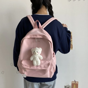 Pink minimalist nylon backpack with plush bear pendant shown on model in school setting