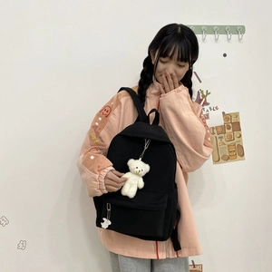 Close-up of a black casual nylon backpack with a cute white bear plush charm on a model