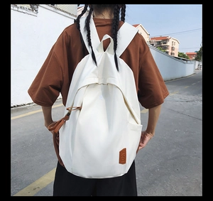 Detail view of white canvas backpack featuring minimal A embroidery and leather day patch