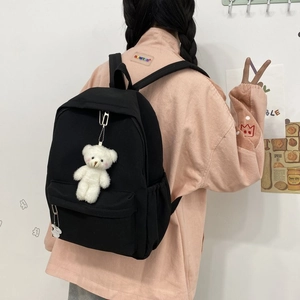 Rear view of model wearing minimalist black nylon backpack with cute bear pendant