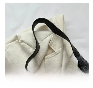 Détail macro du tissu tissé crème et de la bandoulière en cuir noir sur le sac cabas