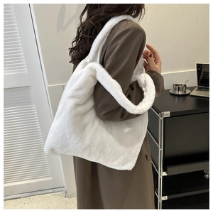 Model wearing a large white plush tote bag with wide shoulder strap in a cozy setting