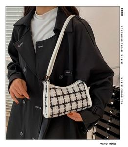 Side view of a black and white plaid tweed shoulder bag worn with a black coat