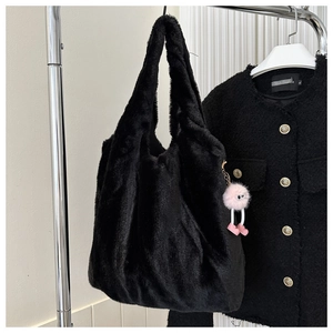 Detail view of the black plush tote bag with a pink monster charm hanging on a rack