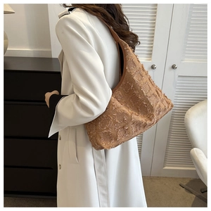 Détail d'un sac porté épaule caramel à carreaux frangés sur un trench-coat blanc