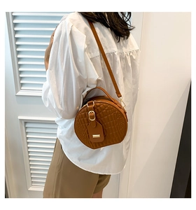 Detail shot of brown quilted round crossbody bag with golden hardware on a model