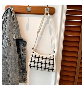 Detail of tweed checkered crossbody bag with white leather trim hanging on a wooden hanger