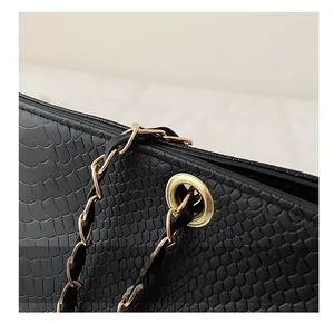 Gros plan des chaînes dorées et de la texture crocodile sur le sac à main noir