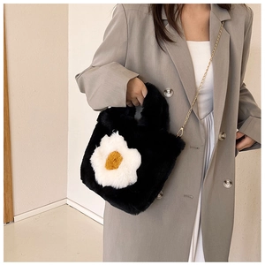 Detail showing plush black faux fur handbag with a white flower charm and golden chain strap