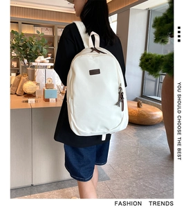 Detail view of stylish white nylon backpack with brown brand label and sturdy shoulder straps