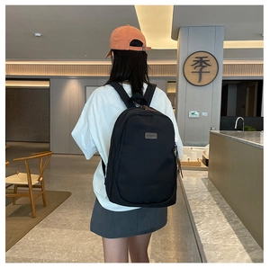 Detail of minimalist black backpack featuring brown leather zipper pull and square patch