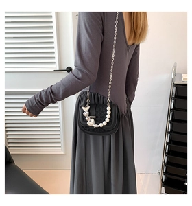 Detail van een mini zwarte crossbody tas met een hartvormige hanger en parelketting