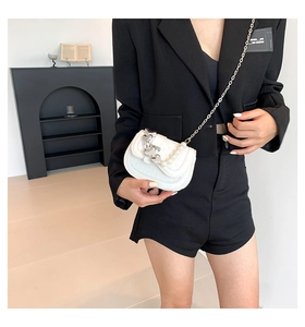 Detail van witte mini-zadeltas met parel hartketting gedragen op een zwarte blazer