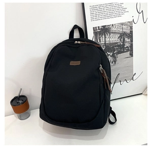 Detail view of black canvas backpack showing the leather brand tag and corded dual zippers