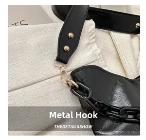 Detalle de bolso saco negro con gancho de metal dorado y cadena acrílica moderna