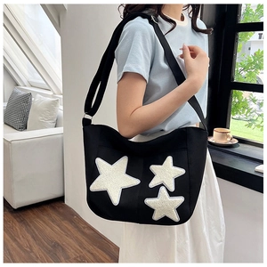 Close-up of black canvas tote bag featuring white chenille star embroidery and wide strap
