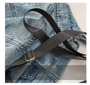 Détail de la bandoulière en nylon noir réglable avec boucle dorée sur sac en denim