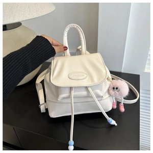 Close-up of cream-colored mini backpack with drawstring closure and pink plush charm