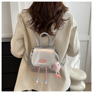 Primer plano de mini mochila plateada con etiqueta rosa y colgante de peluche suave