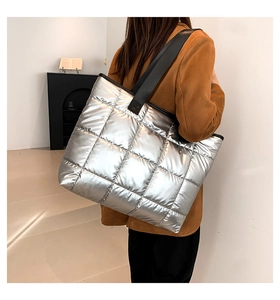 Detalle de un bolso tote acolchado plateado con correa negra llevado por una modelo con traje