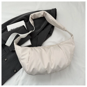 Detail of minimalist beige nylon crescent bag styled with a professional suit and a book