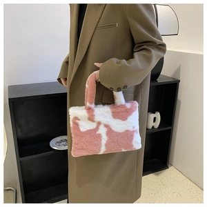 Detail of pink and white cow print plush handbag held by model in stylish brown blazer