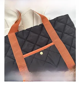 Close-up of quilted black nylon tote bag with orange handles and gold metal buckle detail