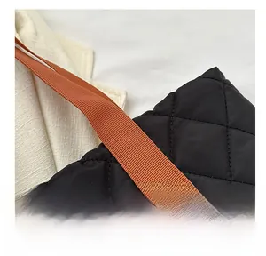 Close-up of black quilted tote bag featuring fine diamond stitching and brown woven strap