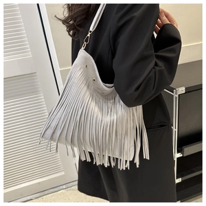 Detail view of grey fringe shoulder bag with suede texture and wide strap on model