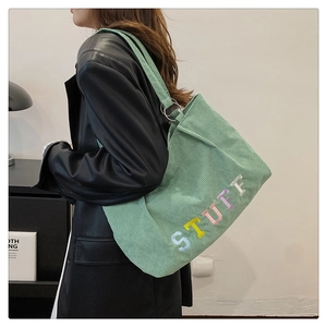 Detail of light green corduroy tote bag with colorful STUFF embroidery on shoulder