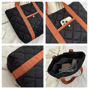 Detail view of black quilted tote bag featuring orange straps and golden snap pocket
