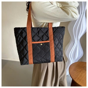 Detail of black quilted tote bag with orange straps and snap pocket on a model