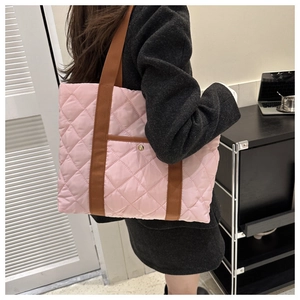 Detail of a large pink quilted tote bag with brown straps and exterior button pocket