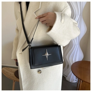 Dettaglio borsa a tracolla nera minimalista con logo a stella d'argento su cappotto avorio