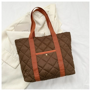 Detail of dark brown quilted tote bag with orange handles and gold snap button pocket